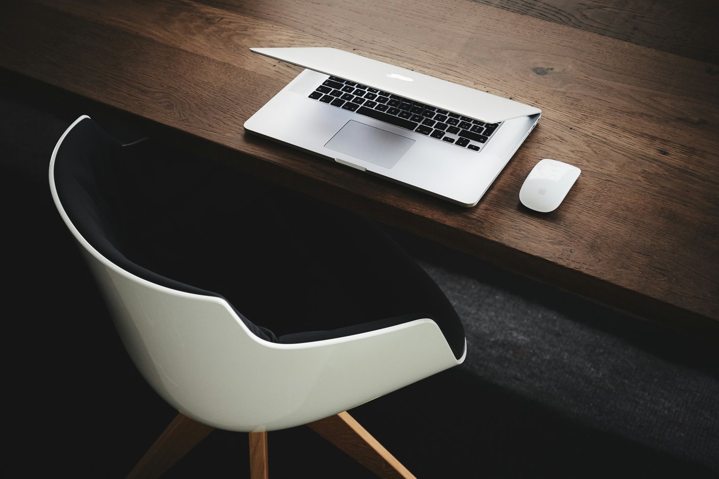 A closed laptop and mouse on a wooden bench beside an empty moulded chair